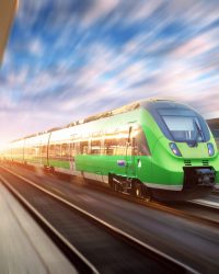 Speed train in motion at the railway station at sunset in Europe. Beautiful green modern train on the railway platform with motion blur effect. Industrial scene with passenger train on railroad